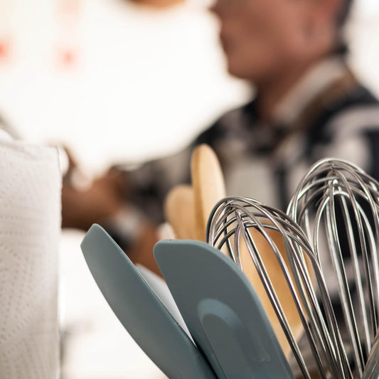 Kitchen utensils including spatulas and whisks in a container with a blurred person in the background.